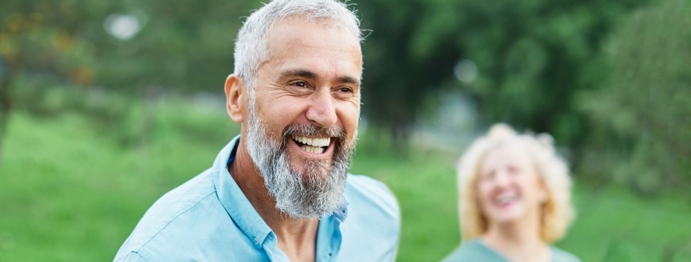 Older man laughing outdoors while walking with woman